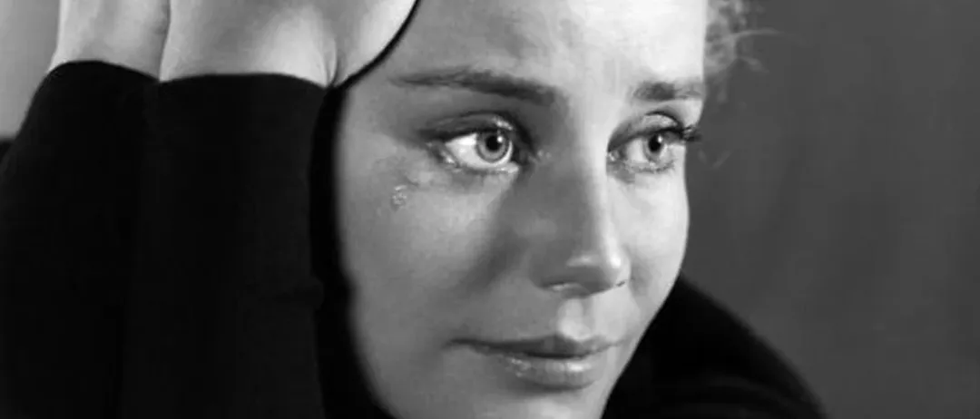 Ein Schwarz-Weiß-Foto zeigt eine Frau mit kurzen Haaren, die ein Rollkragenshirt trägt. Sie hat Tränen in den Augen und hält ihren Kopf mit beiden Händen.