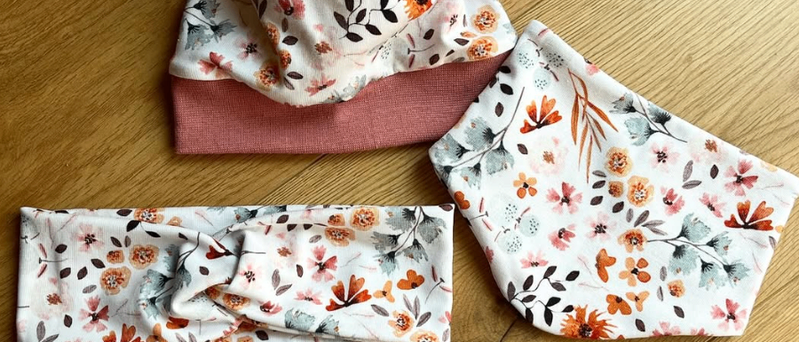 Drei Blumenkopfbänder, eines mit einer Schleife, liegen auf einer Holzoberfläche. Die Kopfbänder haben verschiedene Blumendesigns.