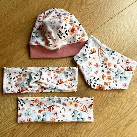 Drei Stücke mit Blumenmuster liegen auf einer Holzoberfläche. Eines ist eine Mütze und die anderen beiden sind Stoffstücke.