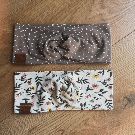 Zwei Stirnbänder auf einer Holzoberfläche. Eines hat ein braunes Punktmuster und das andere ein Blumendesign. Beide haben braune Etiketten.