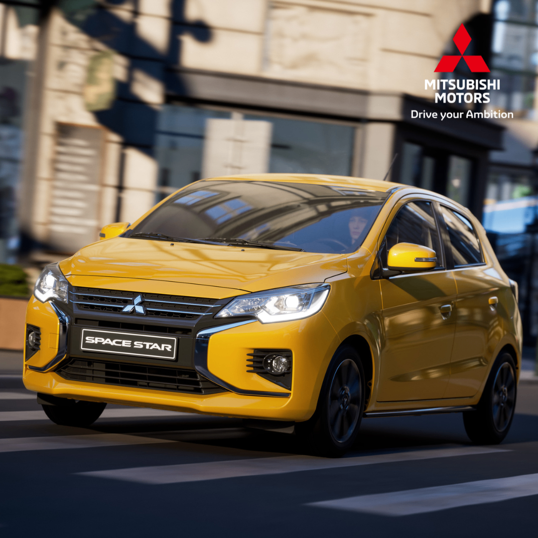 Ein gelbes Mitsubishi Space Star Auto fährt auf einer Stadtstraße. Das Auto zeigt das Mitsubishi Motors Logo und den Markennamen über den Scheinwerfern.
