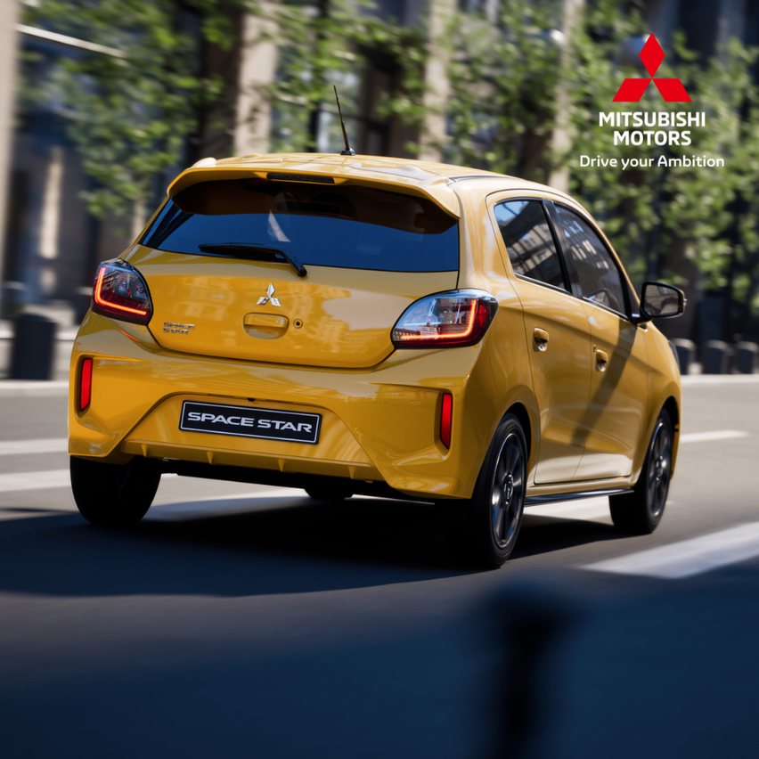 Die Rückseite eines gelben Mitsubishi Space Star fährt auf einer Straße mit Bäumen und einem Mitsubishi Motors Logo.