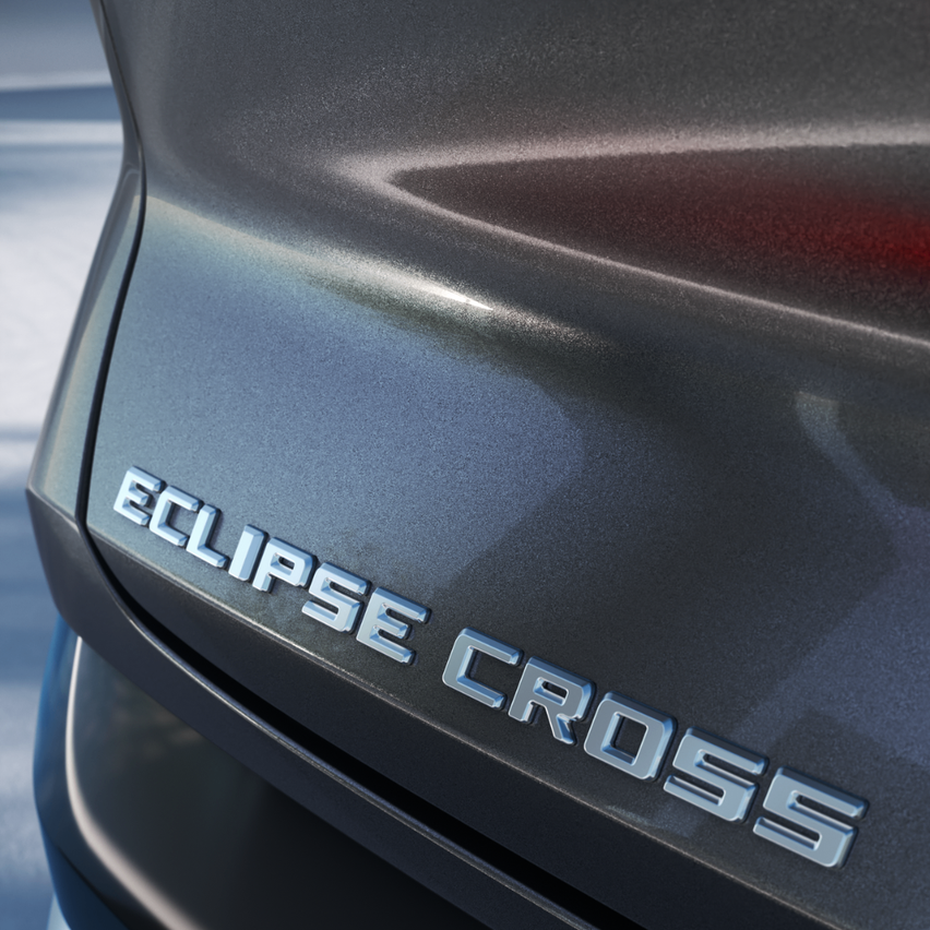 Eine Nahaufnahme des schwarzen Autostoßfängers mit der silbernen Aufschrift 'ECLIPSE CROSS'. Die Oberfläche ist reflektierend.