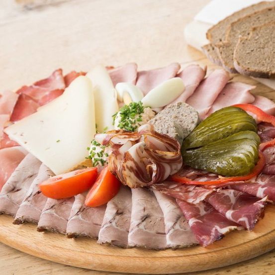 Ein Holzteller mit verschiedenen Fleischsorten, Käse, Tomaten, Gurken und Brot.