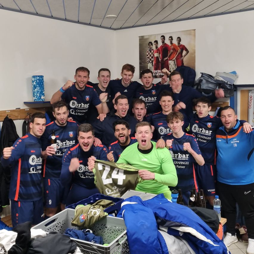 A group of soccer players in blue uniforms celebrate in the locker room, one wearing green. They have 'Berbar' on their jerseys.