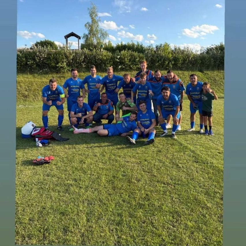 Eine Gruppe von Fußballspielern in blauen Trikots posiert für ein Mannschaftsfoto auf einem Rasenfeld.