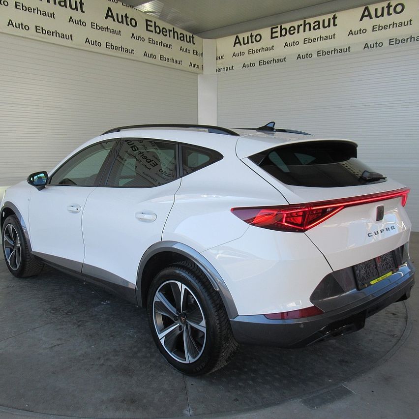 Ein weißer CUPRA SUV steht in einer Garage mit Auto Eberhaut-Schildern an den Wänden. Der SUV hat silberne Räder und ein Nummernschild.