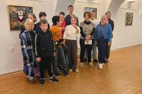 Eine Gruppe von Menschen in einem Raum mit Holzböden und weißen Wänden, einige posieren für ein Foto. Gerahmte Kunstwerke schmücken die Wände.