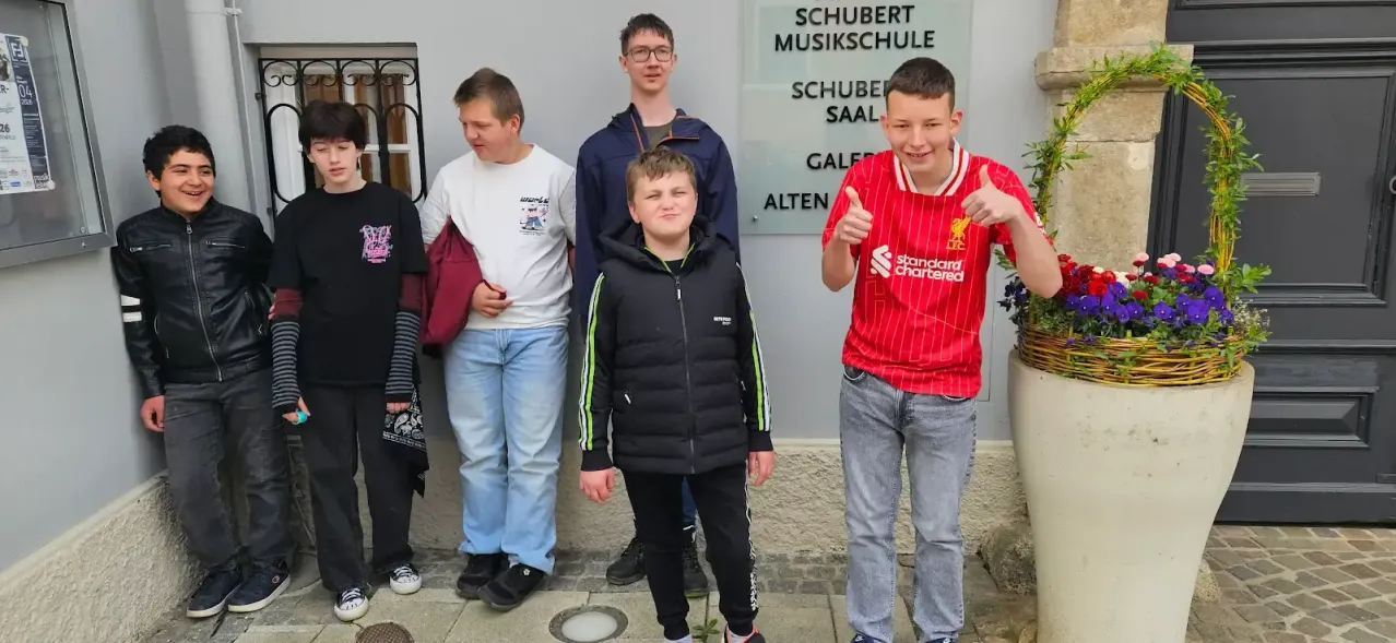 Fünf junge Jungen posieren vor einem Gebäude. Der Junge ganz rechts trägt ein rotes Liverpool-Fußballtrikot. Der Junge in der Mitte trägt eine schwarze Jacke mit grünen Streifen.