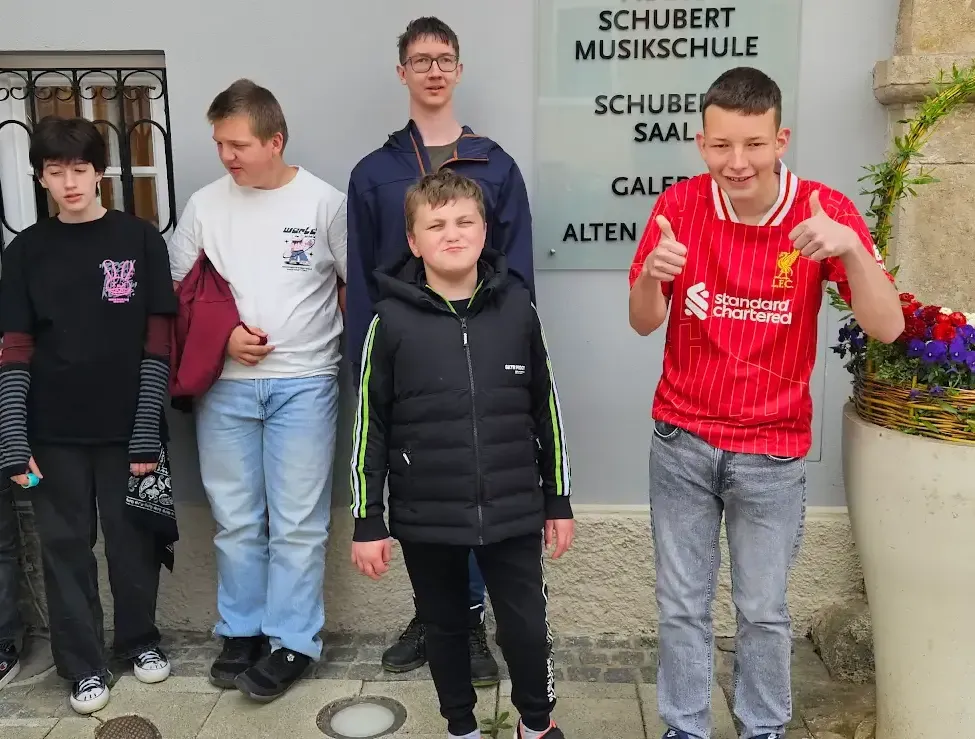 Fünf junge Jungen posieren vor einem Gebäude. Der Junge ganz rechts trägt ein rotes Liverpool-Fußballtrikot. Der Junge in der Mitte trägt eine schwarze Jacke mit grünen Streifen.