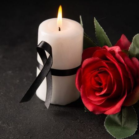 Eine brennende Kerze mit einer schwarzen Schleife und einer roten Rose auf schwarzem Hintergrund.