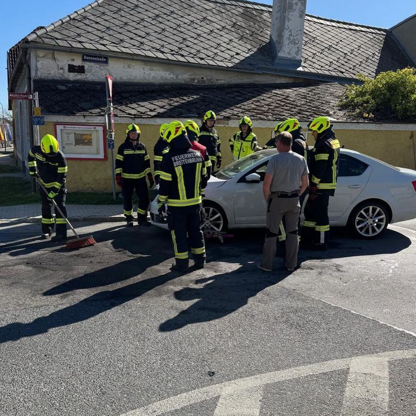 Feuerwehrleute in gelben Helmen sind um ein weißes Auto versammelt. Sie scheinen sich auf einen Vorfall vorzubereiten. Die Umgebung ist sonnig.
