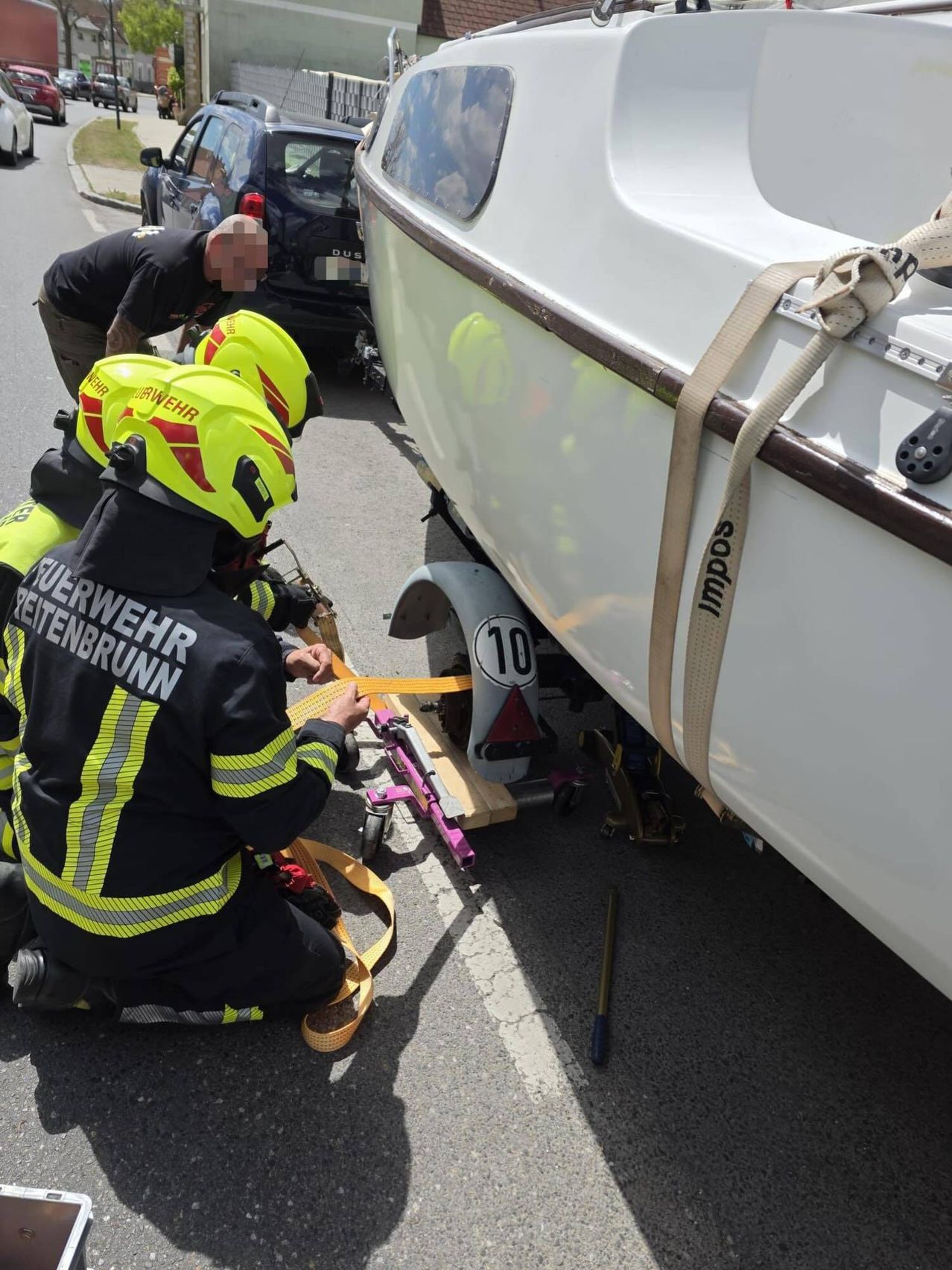 Firefighters in protective gear work to secure a boat to a car. The boat has a number 10 on its rear and is being tied down with straps.