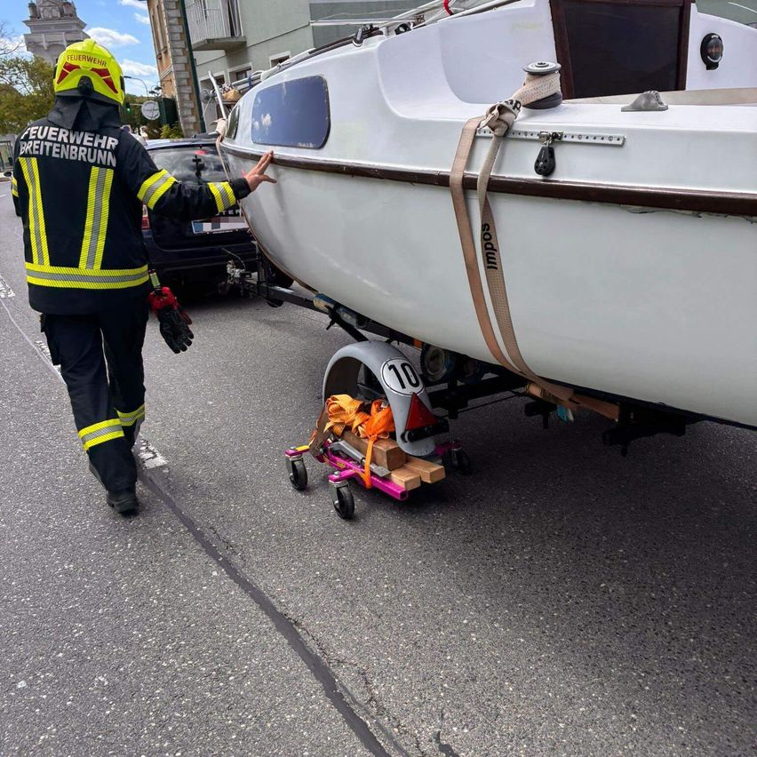 A firefighter is pushing a boat with the number 10 on a trailer along a street.