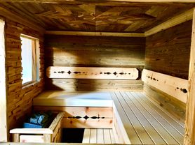 Innenraum einer Holzsauna mit Holzbänken und Wänden. Ein Fenster lässt natürliches Licht herein.
