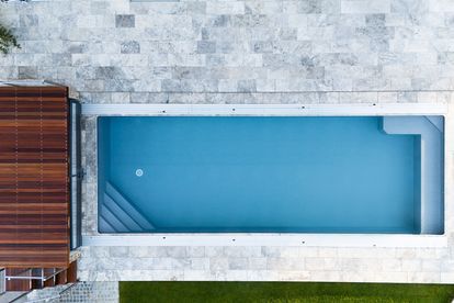 Ein rechteckiger, sauberer Swimmingpool mit blauem Wasser wird von oben gezeigt. Der Pool ist von gefliesten Böden umgeben.