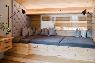Ein Innenansicht eines gemütlichen Holzraums mit Bett, Kissen und Lampe. Das Bett besteht aus Holz und hat blaue Laken.