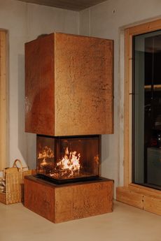 Ein moderner Kamin mit Glasfront, der von warmen orangefarbenen Flammen erhellt wird, steht in einem Raum mit Holzwänden.