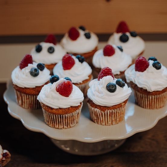 Ein Teller mit Cupcakes mit weißer Glasur, garniert mit roten Beeren und Blaubeeren, ordentlich angeordnet.