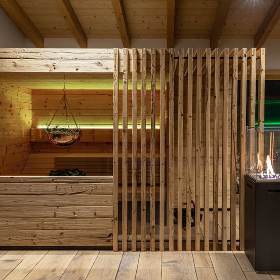 Ein Holzsauna mit Trennwand, hängendem Pflanzentopf und beleuchtetem Kamin. Das Interieur ist gemütlich und warm mit Holzwänden und -böden.