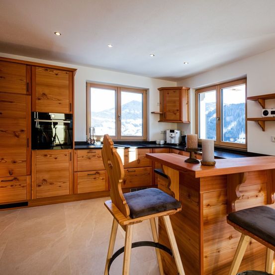 Eine moderne Küche mit Holzschränken, einer Theke und Hockern, mit Blick auf die Berge vor den Fenstern.