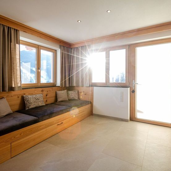 Ein sonniger Raum mit Holzwänden, einem Fenster und einer Bank. Das Sonnenlicht scheint durch das Fenster und erhellt den Raum.