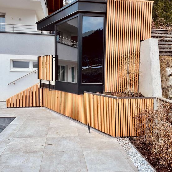 Modernes Haus mit Holzzaun und Glasfenstern, einem kleinen Garten an der Seite und einem kleinen Pool.