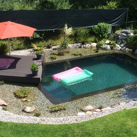 Ein Hinterhof mit einer Holzterrasse, kleinem Pool und Pflanzen. Ein Schirm und eine aufblasbare Schwimmhilfe sind im Pool.