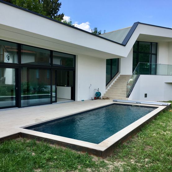 Modernes weißes Haus mit einem großen rechteckigen Pool im Garten, Glastüren und Treppen.