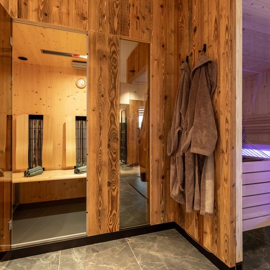 Ein Saunaraum aus Holz mit Spiegeln und Handtüchern. Im Inneren hat eine Bank zwei Handtücher. Eine Klimaanlage ist an der Decke.