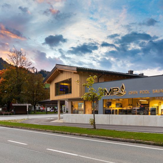 Ein modernes Gebäude mit MP-Logo und offenem Pool-Sauna an der Straße. Der Himmel ist bewölkt und die Sonne geht hinter den Bergen unter.