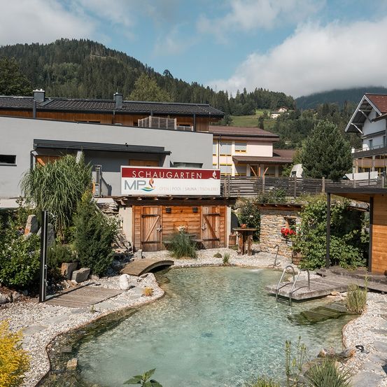 Ein Resort mit offenem Pool und Sauna, Schaugarten, umgeben von Bergen und Grün. Holzstrukturen und eine Brücke erhöhen seinen Charme.