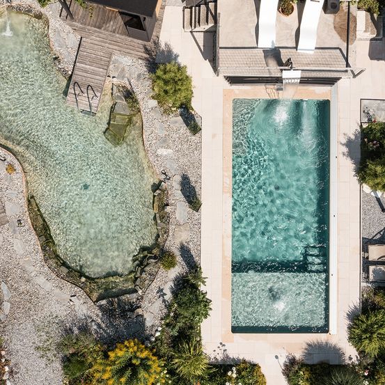 Ein Luftbild eines Landhauses mit zwei Pools. Ein Pool hat einen kleinen Wasserfall. Zwei Liegestühle sind auf der Terrasse.