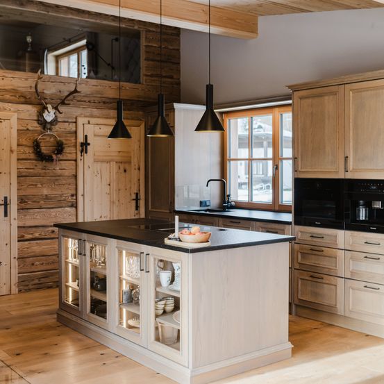 Eine Küche mit Holzwänden, einer großen Insel mit Glastüren, einer schwarzen Arbeitsplatte und einem Fenster mit Holzrahmen.