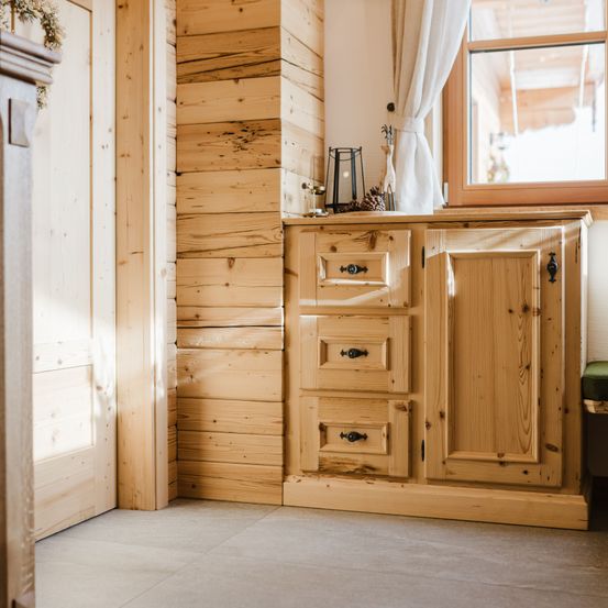Ein kleiner Holzschrank mit drei Schubladen und einem Fenster darüber. Die Wand besteht aus Holzplanken.
