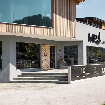 Ein modernes Gebäude mit einer Holztür und Glasfenstern. Es hat ein Schild mit dem Text '15 Jahre' und einem Kranzdesign über der Tür.