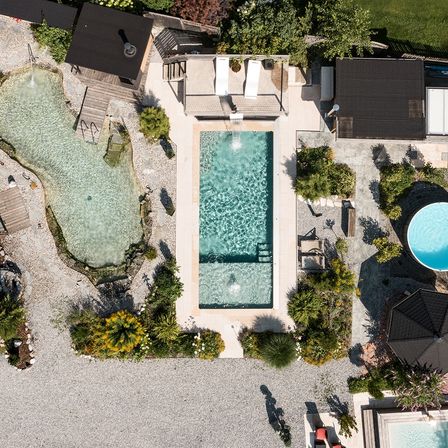 Eine Luftaufnahme eines Resorts mit zwei Swimmingpools, einem Loungebereich und einem Pavillon. Das Gebiet ist von Pflanzen und Bäumen umgeben.