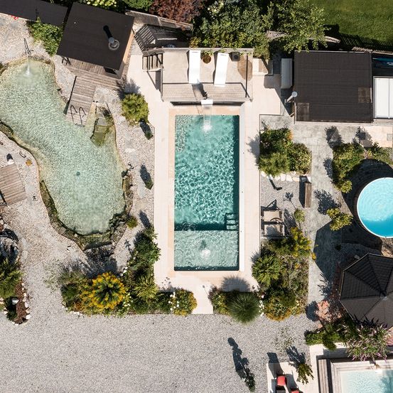 Eine Luftaufnahme eines Resorts mit zwei Swimmingpools, einem Loungebereich und einem Pavillon. Das Gebiet ist von Pflanzen und Bäumen umgeben.