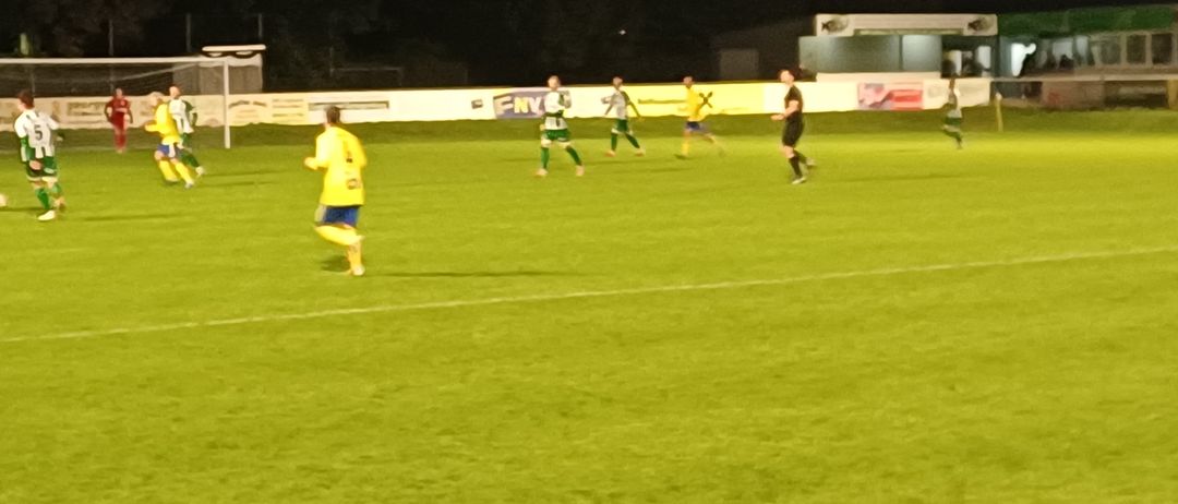Ein Nachtfußballspiel mit Spielern in gelben und grünen Trikots, die auf dem Feld unter Flutlichtern laufen.