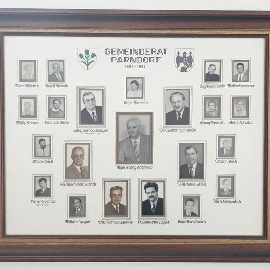 Ein gerahmter Collage von 20 Porträts von Männern in Anzügen, mit ihren Namen und Titeln beschriftet, vom Gemeinderat Parndorf 1987-1992.