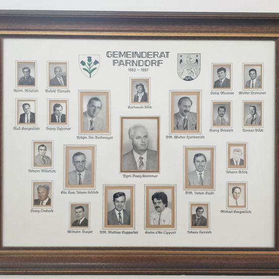 Ein gerahmtes Collage aus 16 Schwarz-Weiß-Fotos von Personen, angeordnet in drei Reihen, mit dem Titel 'Gemeinderat Parndorf 1982-1987' oben. Jedes Foto ist mit dem Namen der Person beschriftet.