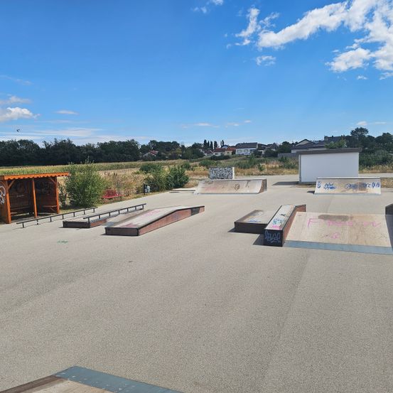 Ein leerer Skatepark mit klarem blauem Himmel, mit verschiedenen Rampen und Graffiti auf Betonflächen.
