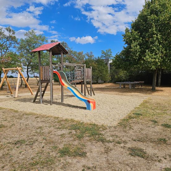Ein Kinderspielplatz mit Rutsche und Klettergerüst unter blauem Himmel mit Wolken.