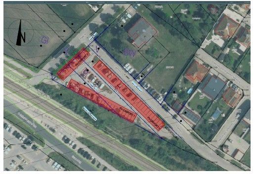 Eine Luftaufnahme eines Grundstücks mit einem markierten Parkplatz, umgeben von Straßen und Grünflächen. Der Parkplatz ist rot hervorgehoben, und verschiedene Gebäude und Strukturen sind sichtbar.