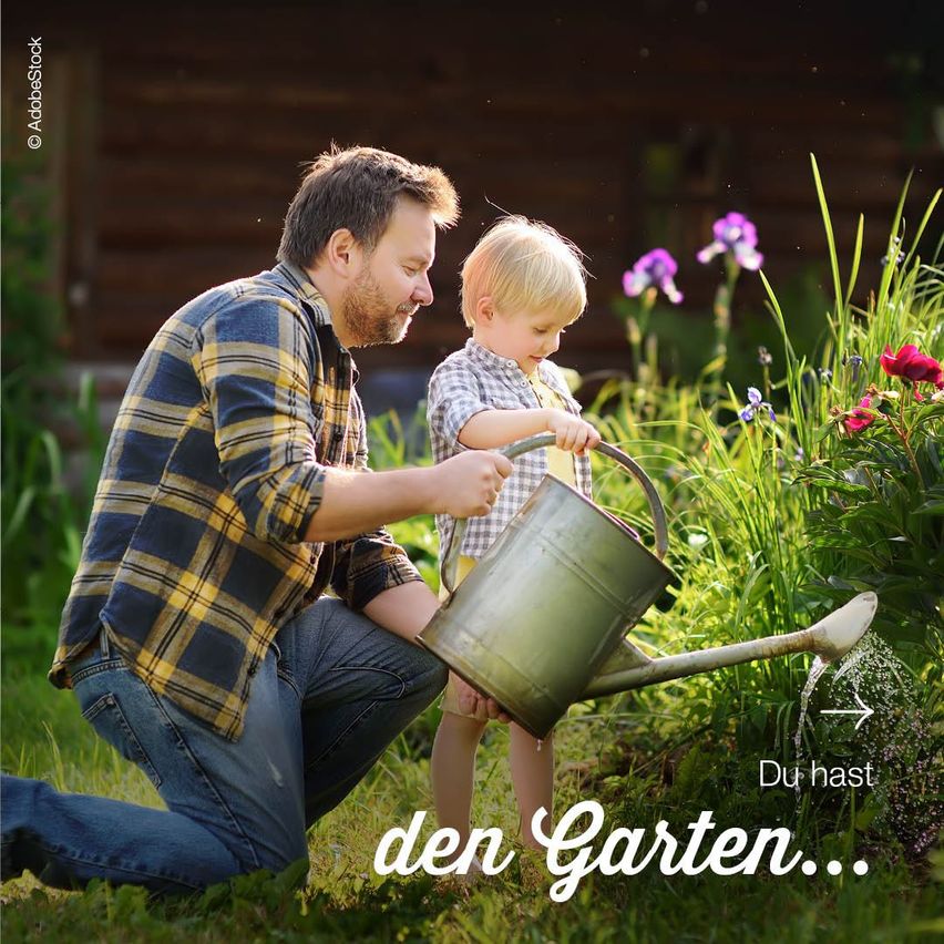 Ein Mann und ein Junge gießen Pflanzen in einem Garten. Der Junge hält eine Gießkanne. Sie lächeln und genießen die Aktivität.