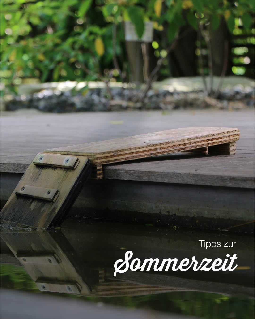 Eine Holzplatte mit einem Scharnier ist teilweise in Wasser auf einer Holzterrasse eingetaucht. Das Bild enthält auch eine Reflexion der Holzplatte.