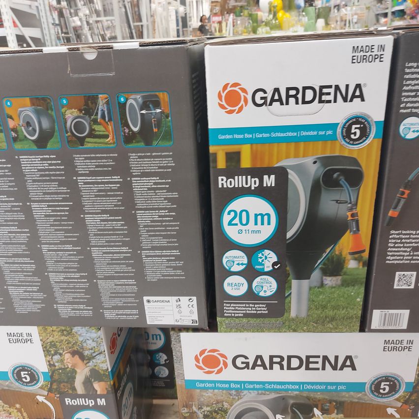 Ein Ladendisplay von GARDENA RollUp M Gartenschlauchboxen. Die Boxen sind übereinander gestapelt, wobei eine prominent die RollUp M-Markenwerbung und -Spezifikationen zeigt.