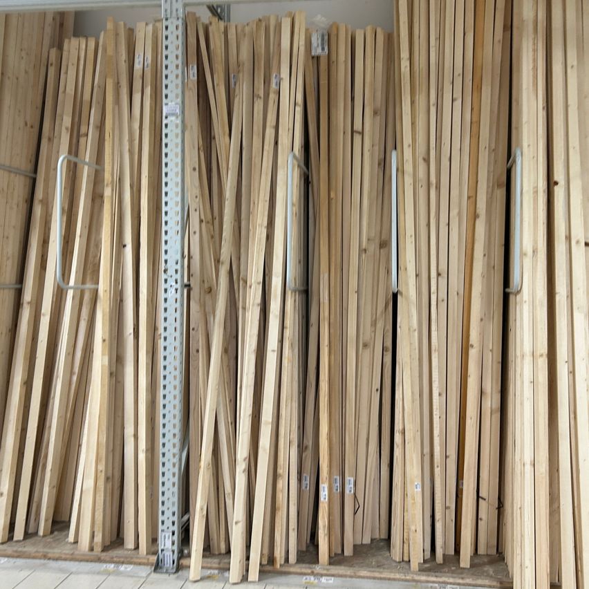 Reihen von Holzbrettern sind ordentlich gestapelt an einer Wand, mit weißen Etiketten an einigen befestigt. Sie sind auf eine Weise organisiert, die auf ein Lager oder ein Lagerhaus hinweist.