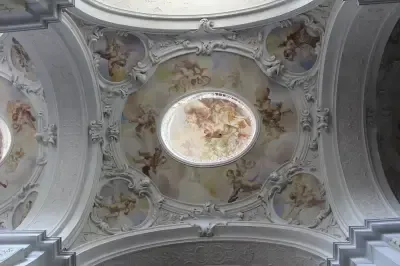 Das Innere einer Kirche zeigt eine Kuppeldecke mit komplizierten Mustern und Gemälden. Die Kuppel ist rund und von aufwendigen, verzierten Dekorationen umgeben.