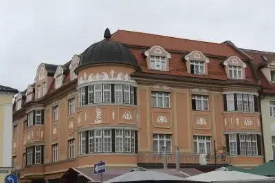 Ein großes, kunstvoll gestaltetes Gebäude mit einem roten Dach und einer Kuppel, ausgestattet mit vielen Fenstern und dekorativen Elementen. Es befindet sich in einem geschäftigen städtischen Bereich mit anderen Gebäuden und Straßenschildern im Sichtfeld.